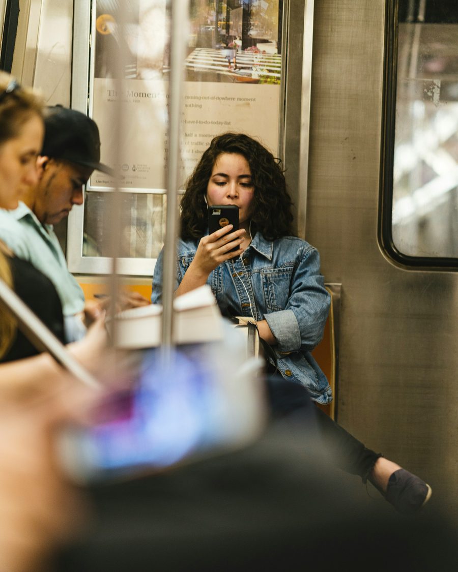 Una persona mira su teléfono junto a la ventanilla de un tren, con más pasajeros de fondo